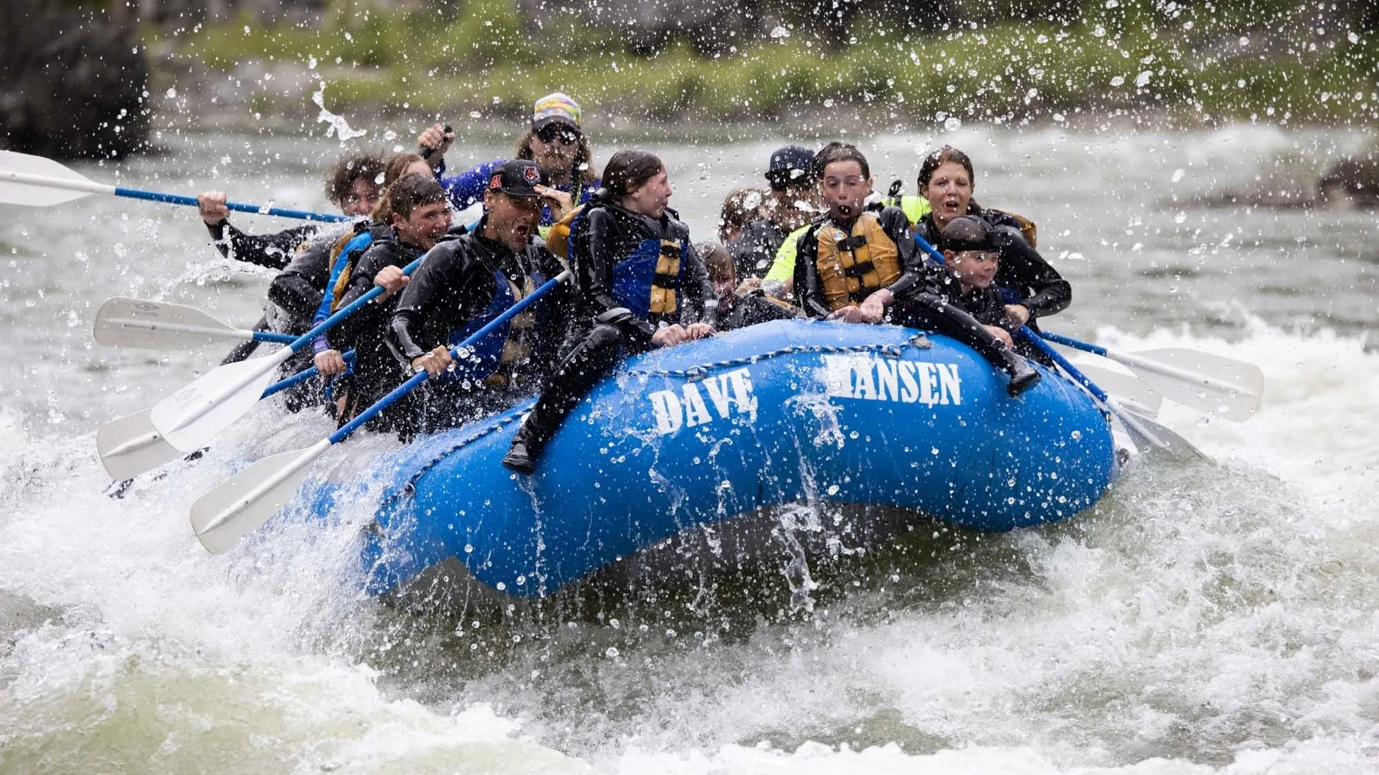 Two children ride on the front of a blue Dave Hansen Whitewater raft as they paddle through a whitewater rapid.