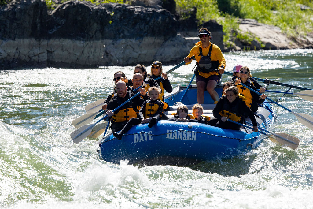 A group of children and adults paddling a blue Dave Hansen Whitewater raft through whitewater rapids on the Snake River.
