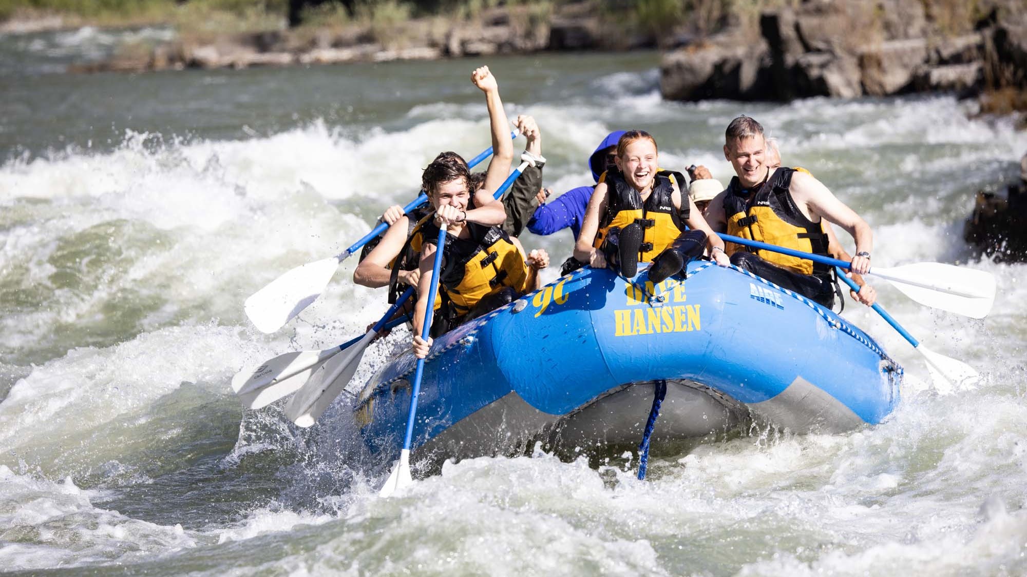 A young girl rides on the front of a blue Dave Hansen Whitewater raft as they paddle through a whitewater rapid.