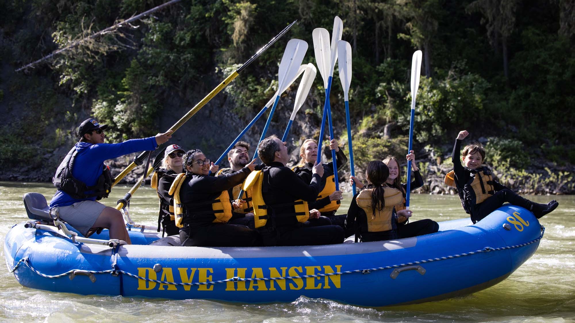 A group of whitewater rafters raise their paddles in a 