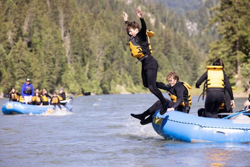 A client jumps off a blue raft and into the water while floating down the Snake River with Dave Hansen Whitewater.