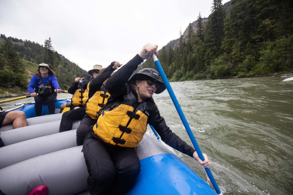 An older woman helps paddle a blue raft down the Snake River on a rainy day in Jackson Hole.