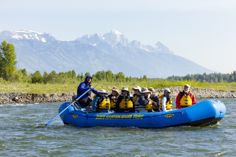 A blue Dave Hansen Whitewater raft floating down a scenic section of the Snake River under the Tetons mountains.