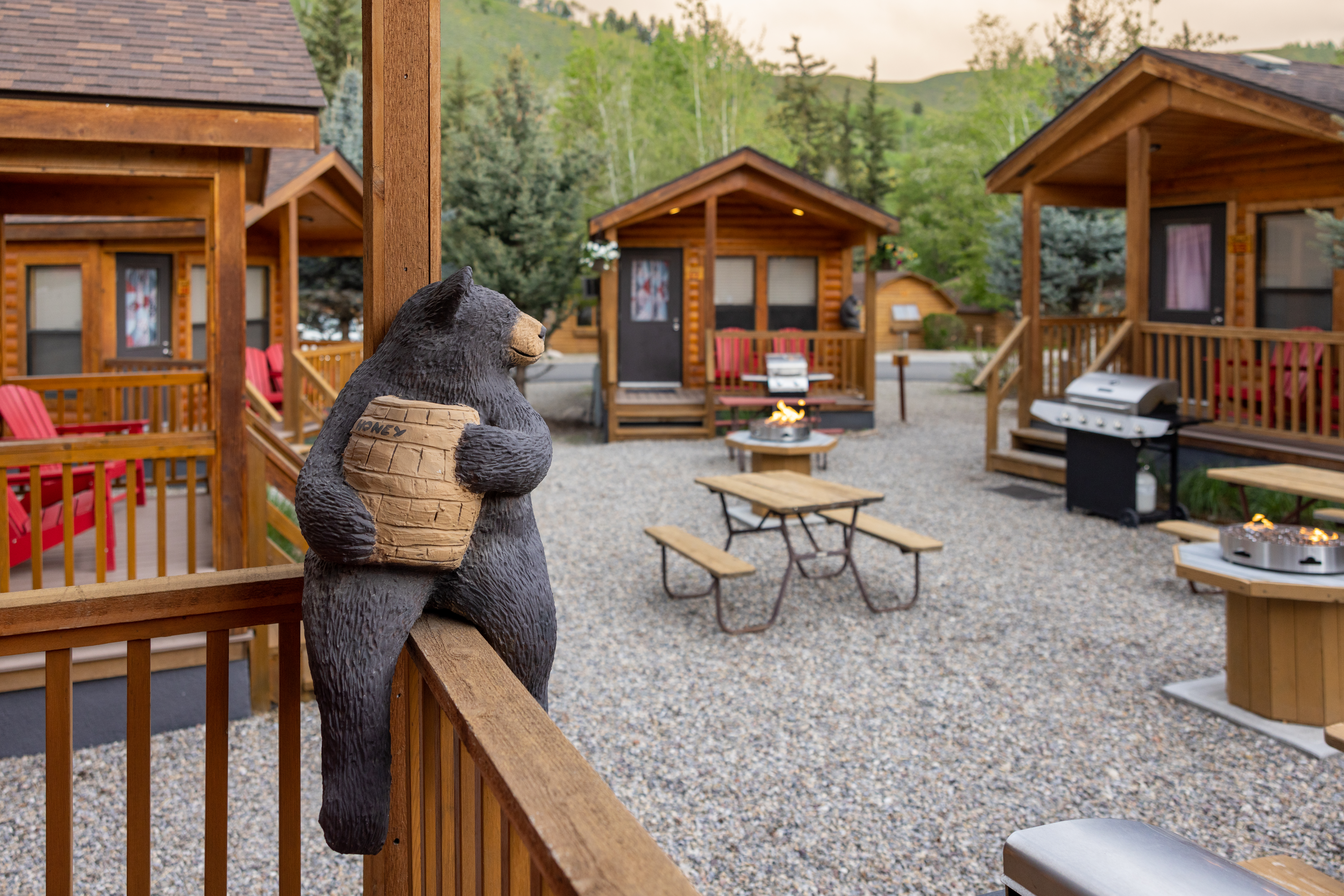 A statue of a black bear holding a jar of honey perched on the porch of a log cabin at Snake River Cabins & RV Village.