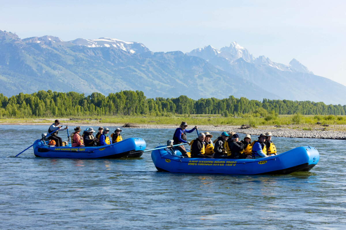 Two Dave Hansen River Trips rafts floating side by side on the Snake River with the snow-capped Grand Teton mountains rising dramatically in the background on a clear summer day.