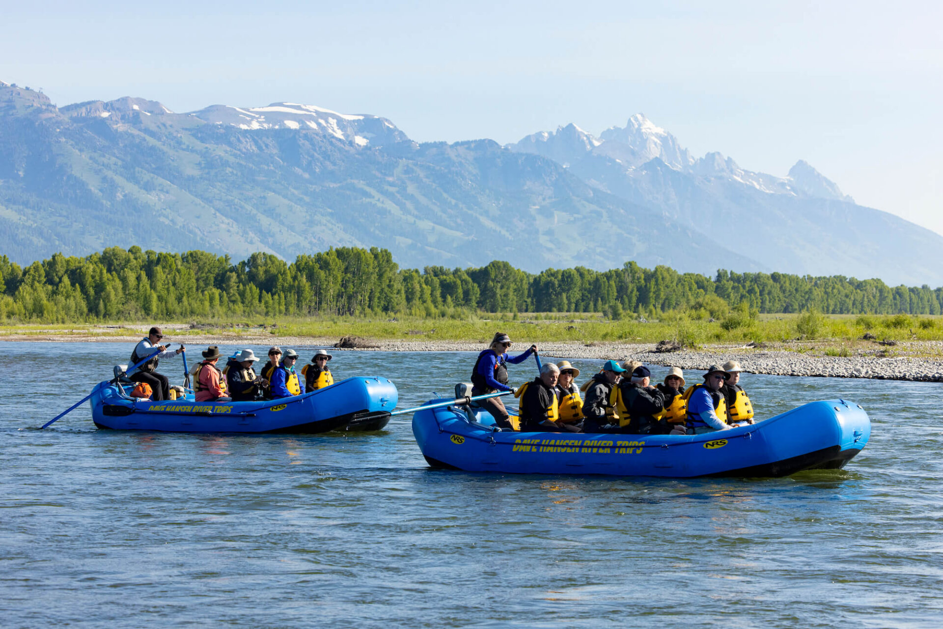 Two Dave Hansen River Trips rafts floating side by side on the Snake River with the snow-capped Grand Teton mountains rising dramatically in the background on a clear summer day.