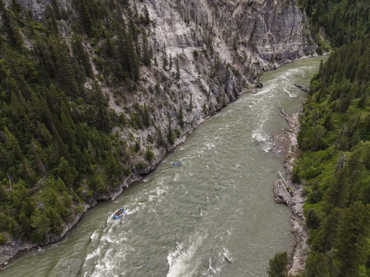 Aerial drone photo of two Dave Hansen rafts navigating whitewater rapids deep inside the Snake River Canyon, surrounded by towering grey rock walls and dense forest.