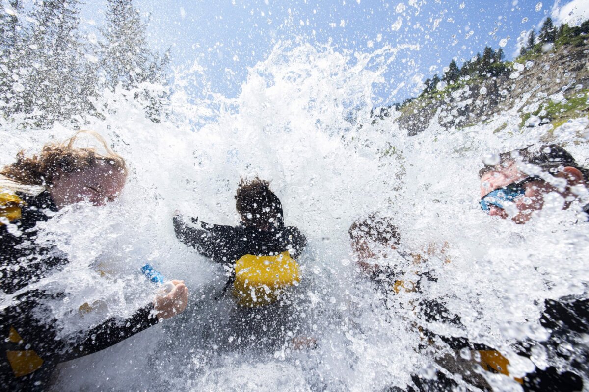 A close-up action shot of rafters on a Dave Hansen trip being completely engulfed by a whitewater wave in the Snake River Canyon, water spraying in all directions on a sunny day.