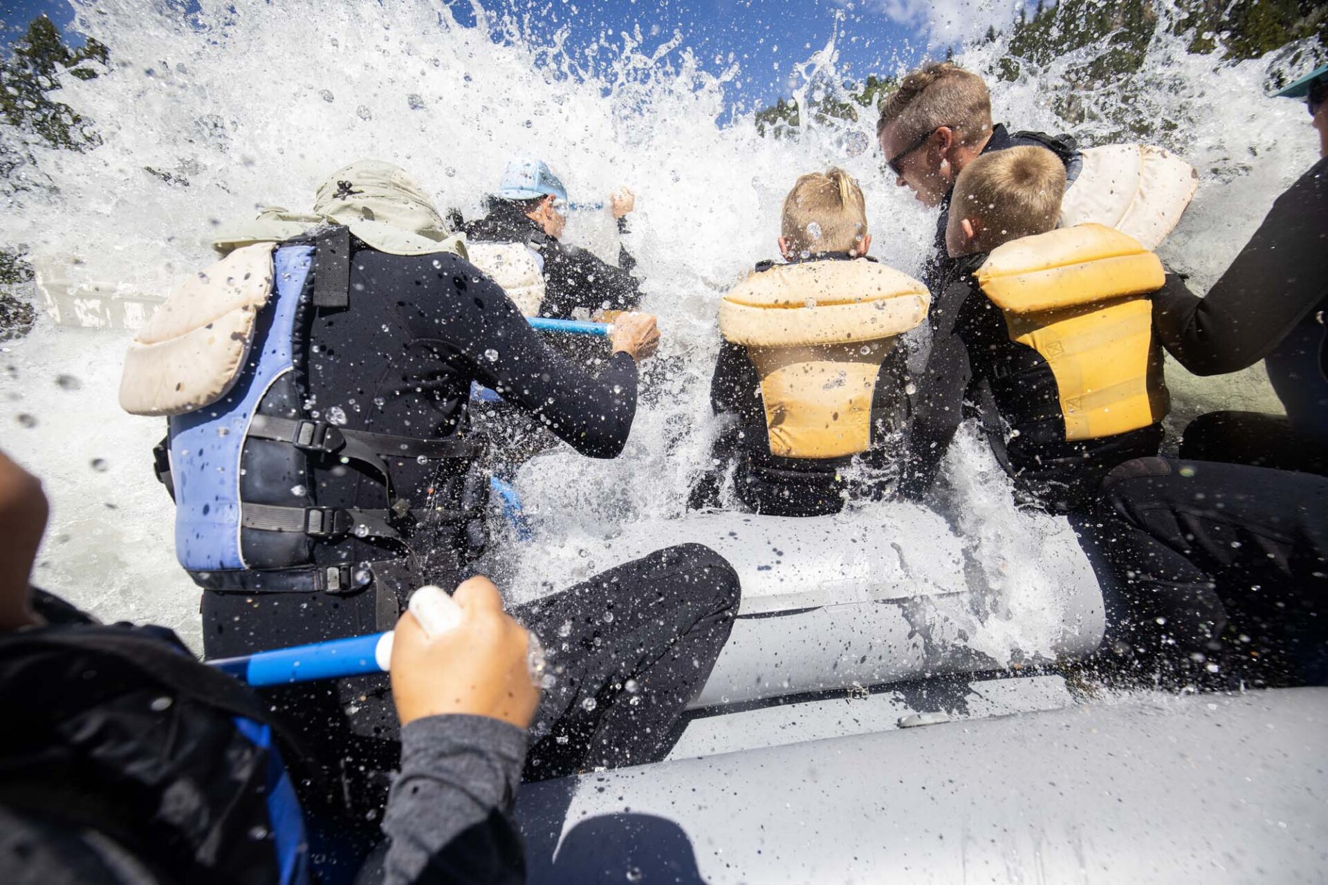 Point-of-view shot from inside a Dave Hansen raft as a massive wave crashes over the bow, soaking rafters in yellow and blue life jackets on the Snake River Canyon whitewater trip.