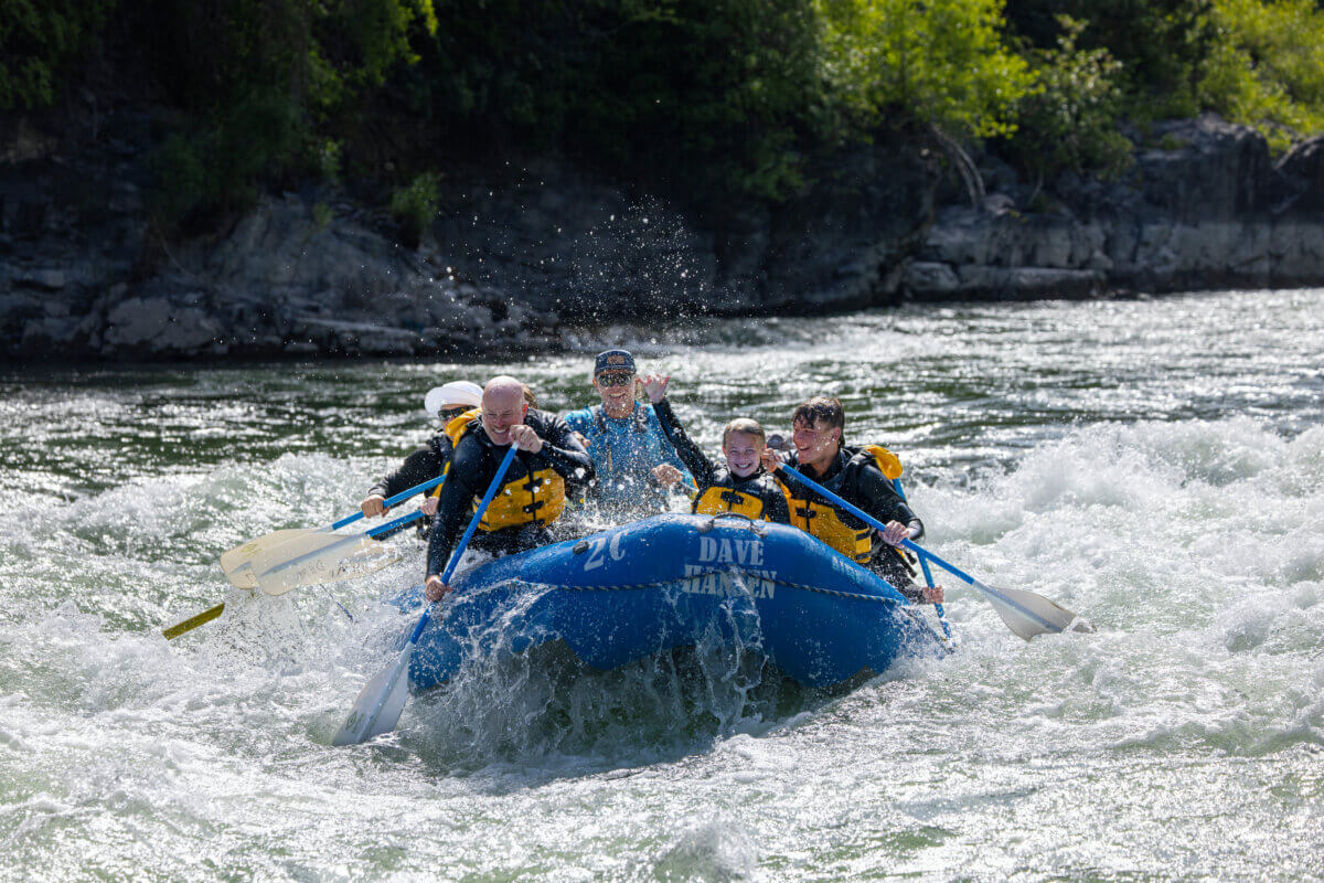 A family smiling and cheering while whitewater rafting through waves on the Snake River with a Dave Hansen Whitewater guide in Jackson Hole, Wyoming