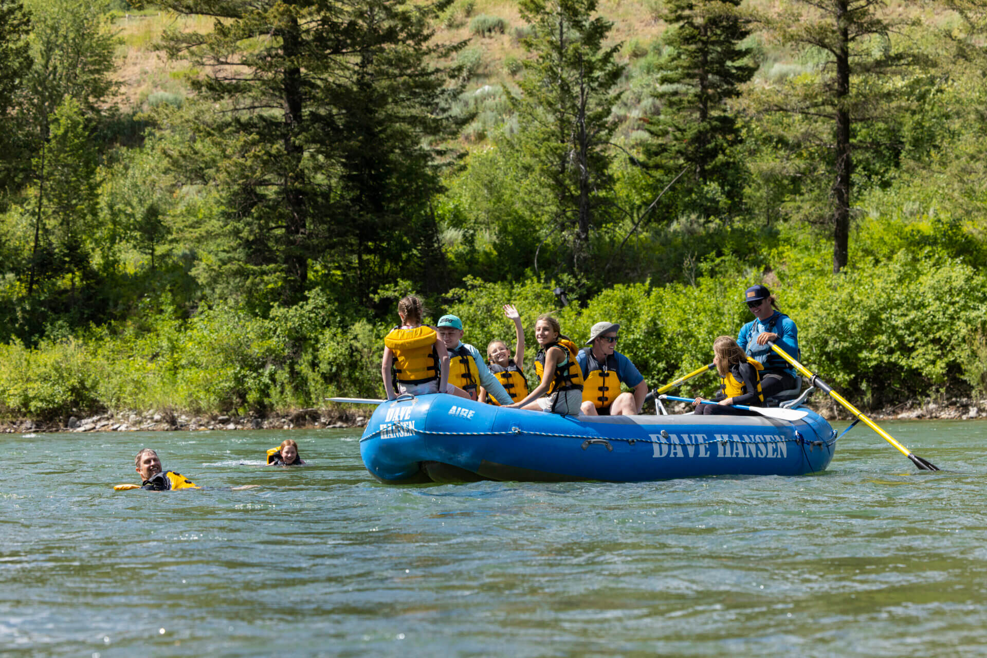 A family and guide on a blue Dave Hansen Whitewater raft swimming in the Snake River