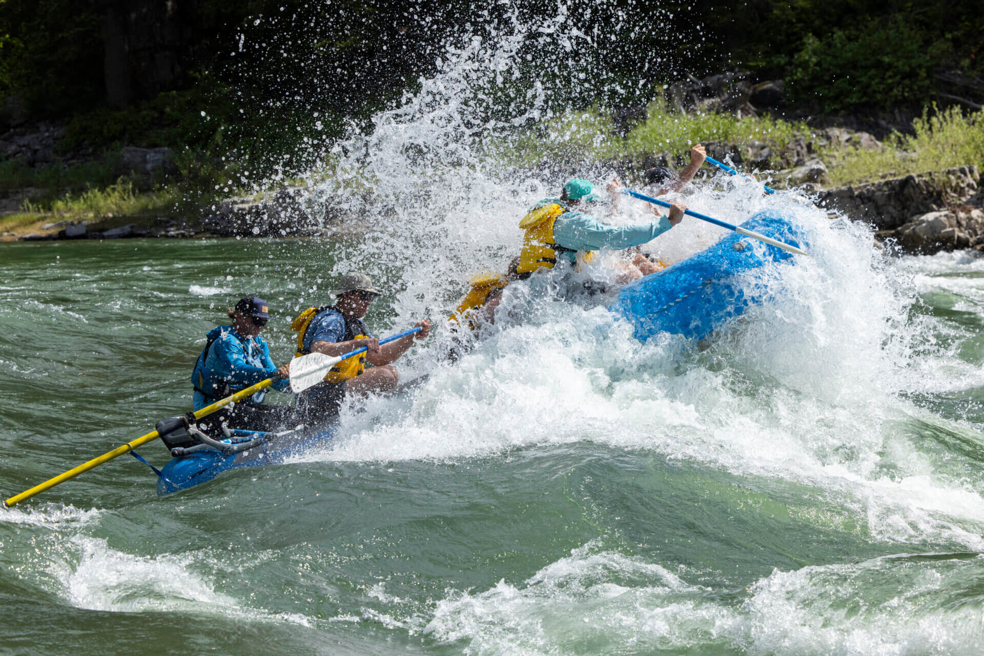 A blue Dave Hansen Whitewater raft crashing through a massive, splashing wave on the Snake River.